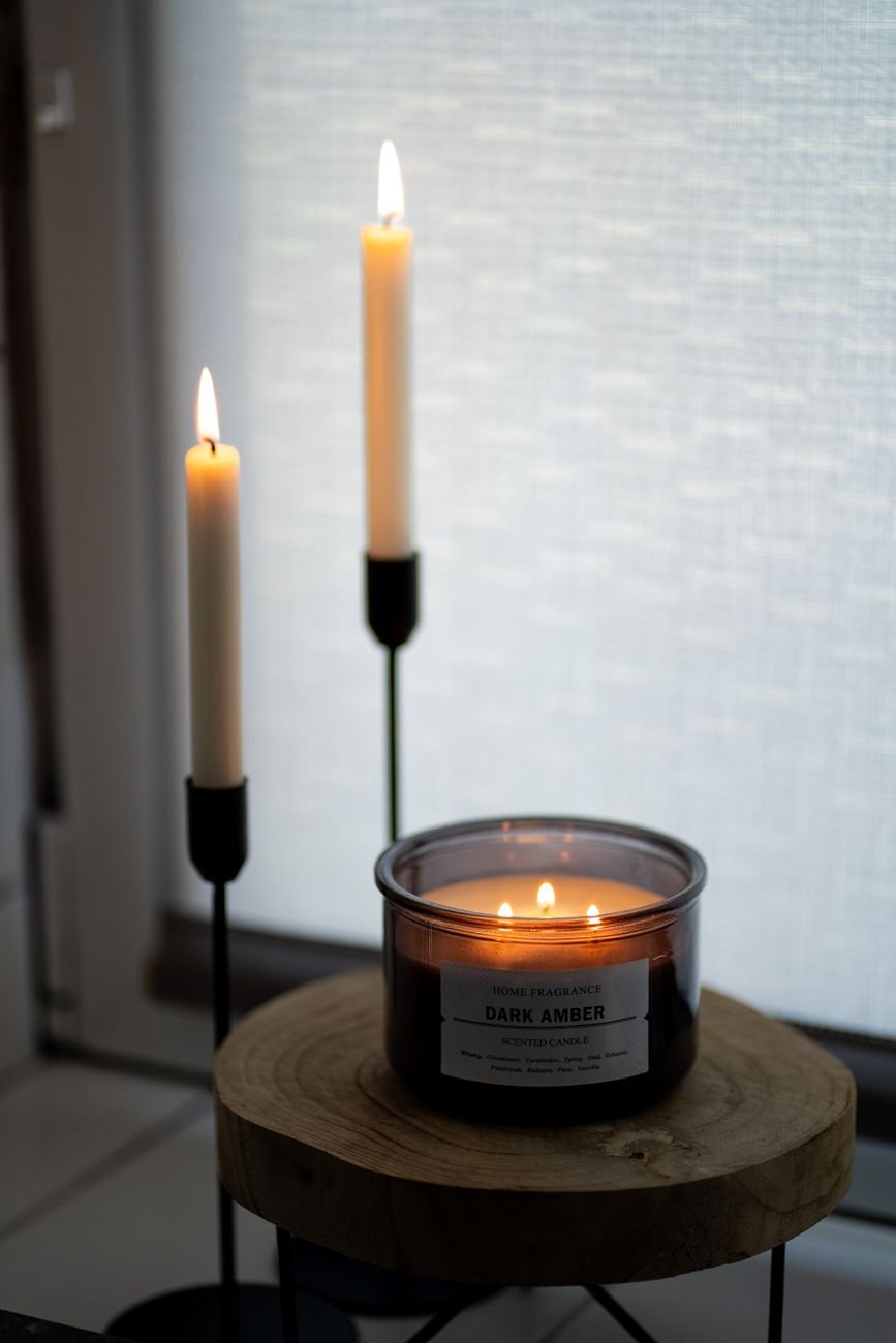 Illuminated dark amber candle with elegant candlesticks creating a warm ambiance indoors.